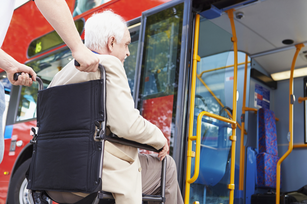 Support working pushing wheelchair with elderly man in it onto a bus.